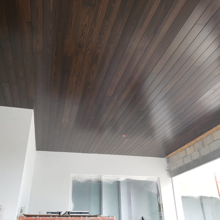 Dark-stained tongue-and-groove ceiling installed above a large opening.
