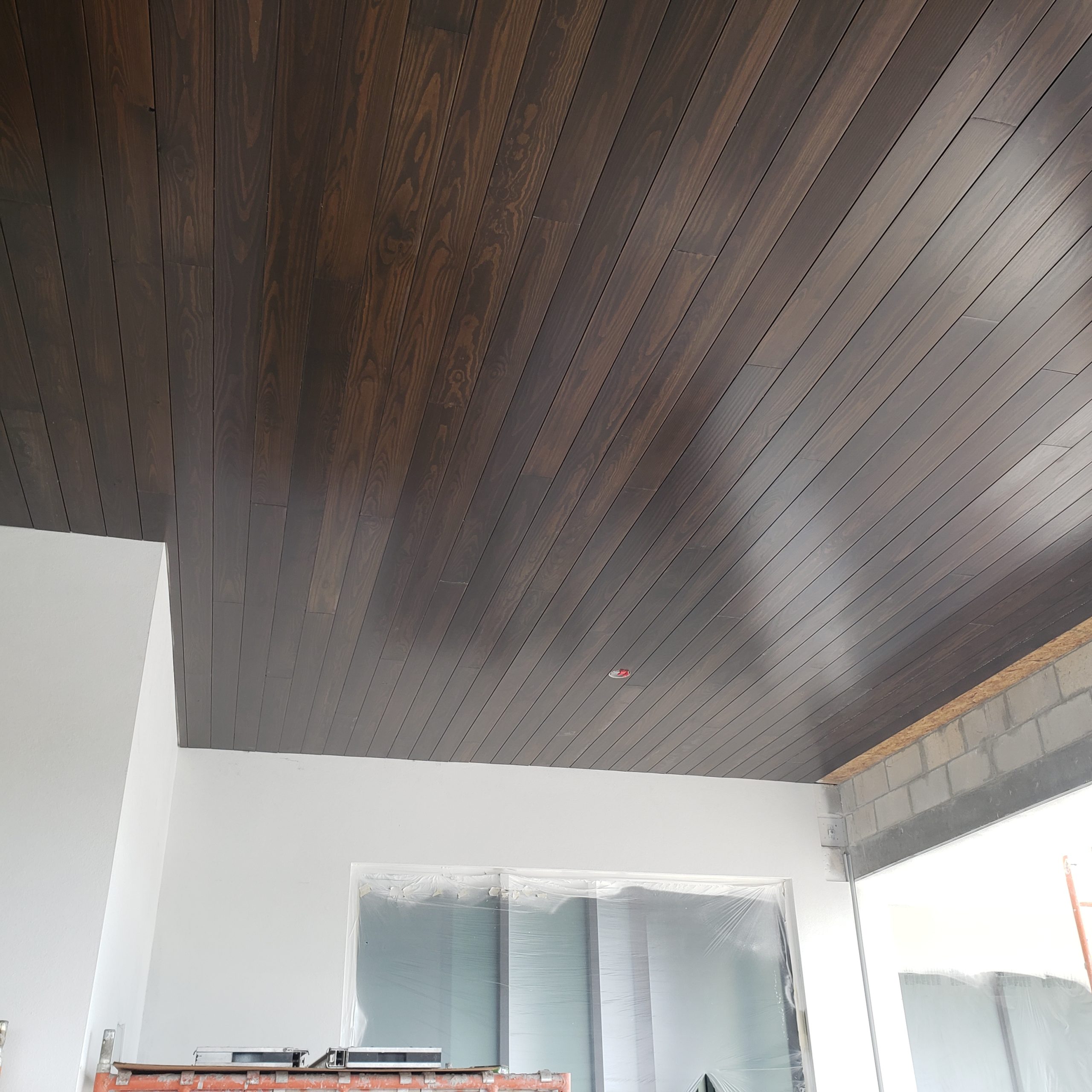 Dark-stained tongue-and-groove ceiling installed above a large opening.