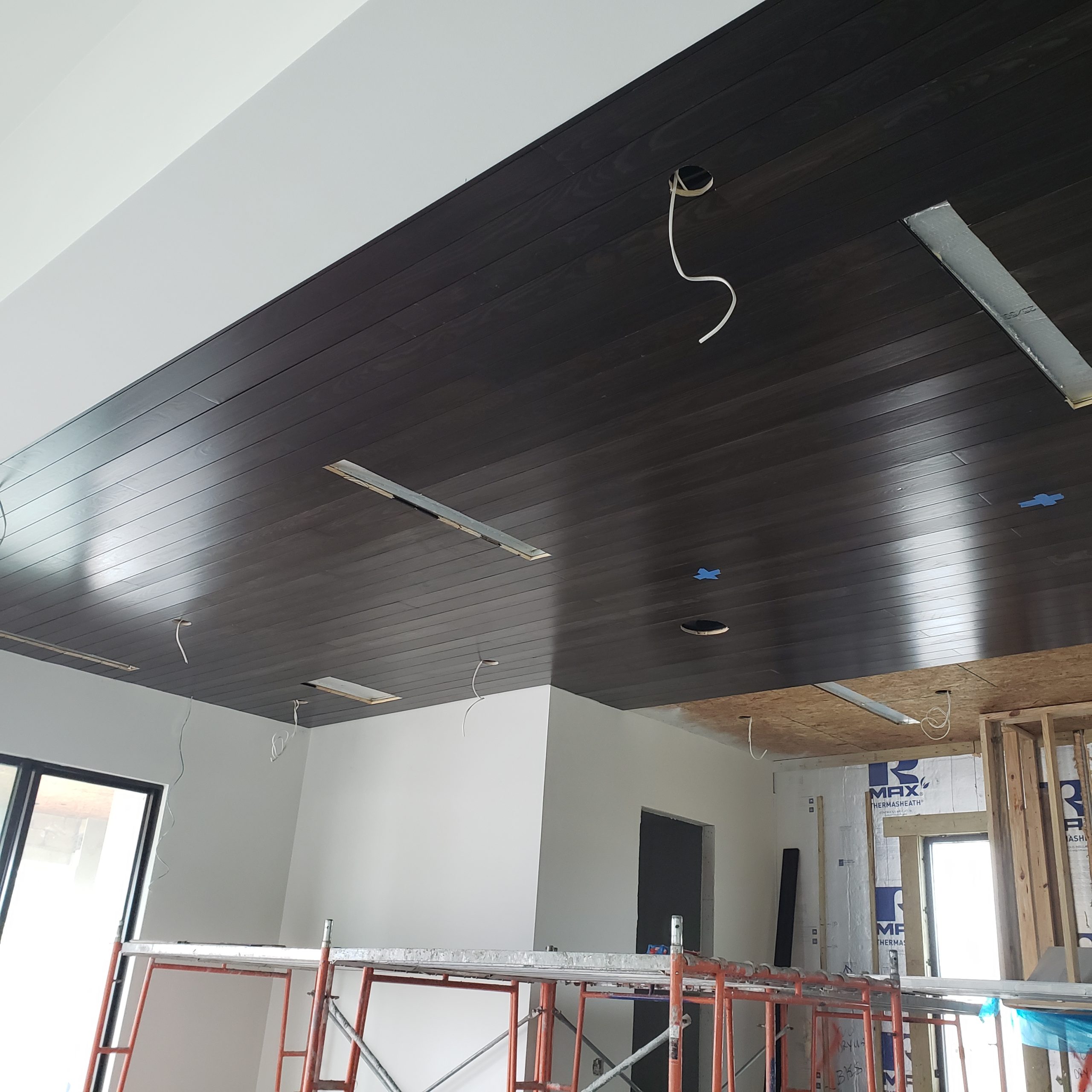 Dark-stained tongue-and-groove ceiling being installed over scaffolding