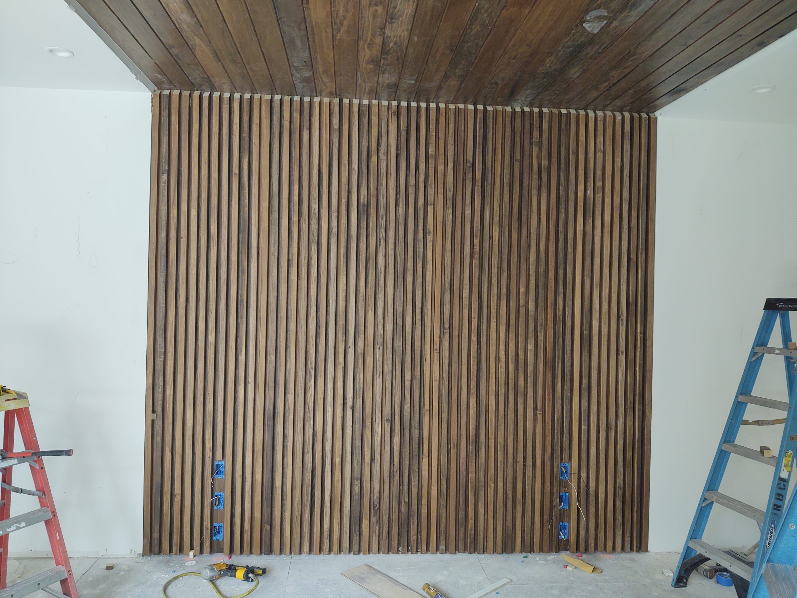 Wood slat wall and ceiling being installed in a room under construction