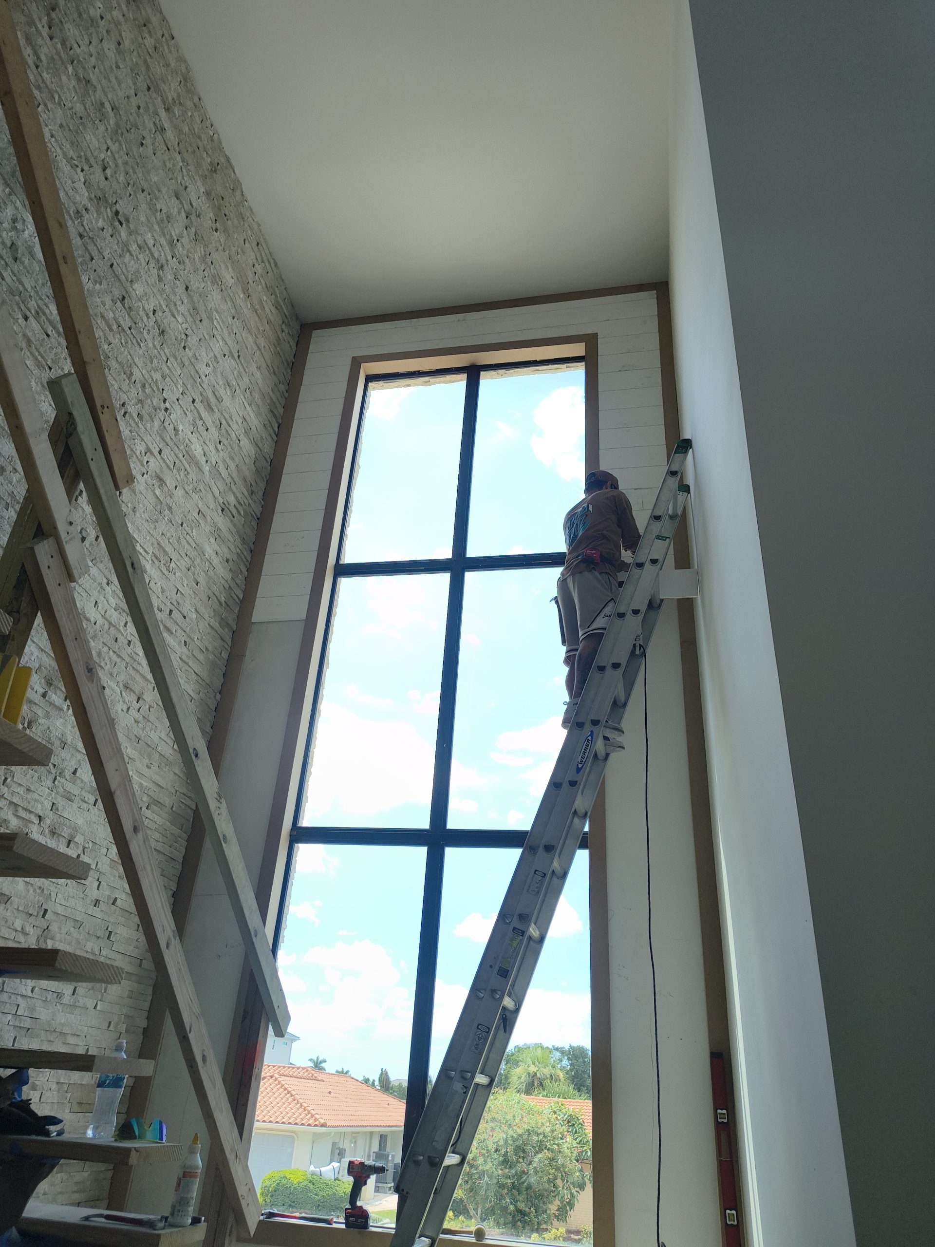 Two-story tongue-and-groove wall surrounding a tall window beside a stone accent wall.