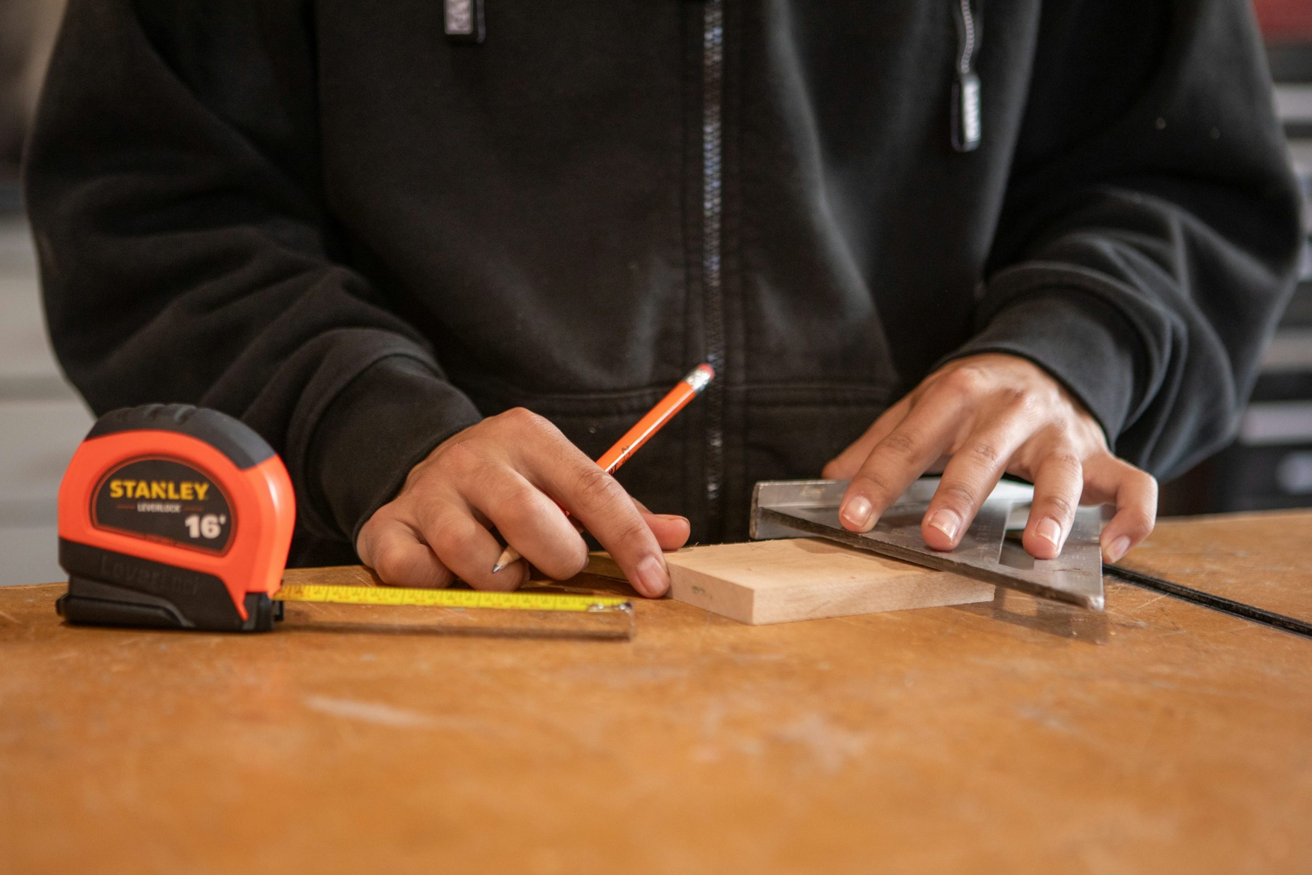Hands measuring and marking wood with a pencil and square during woodworking project planning