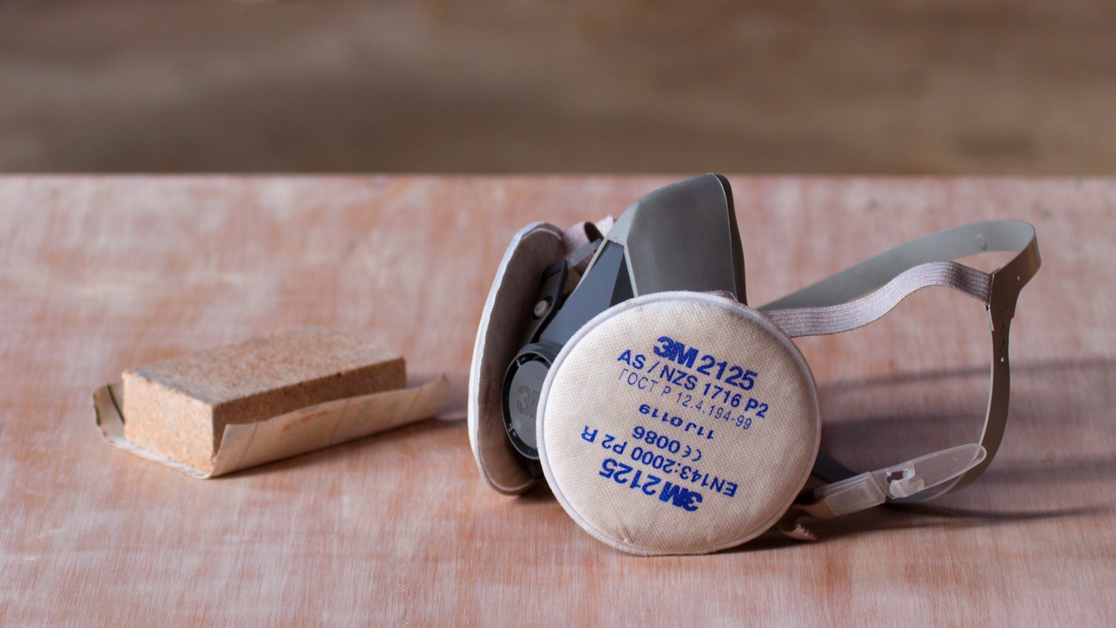 Half-face respirator beside a sanding block on a woodworking surface
