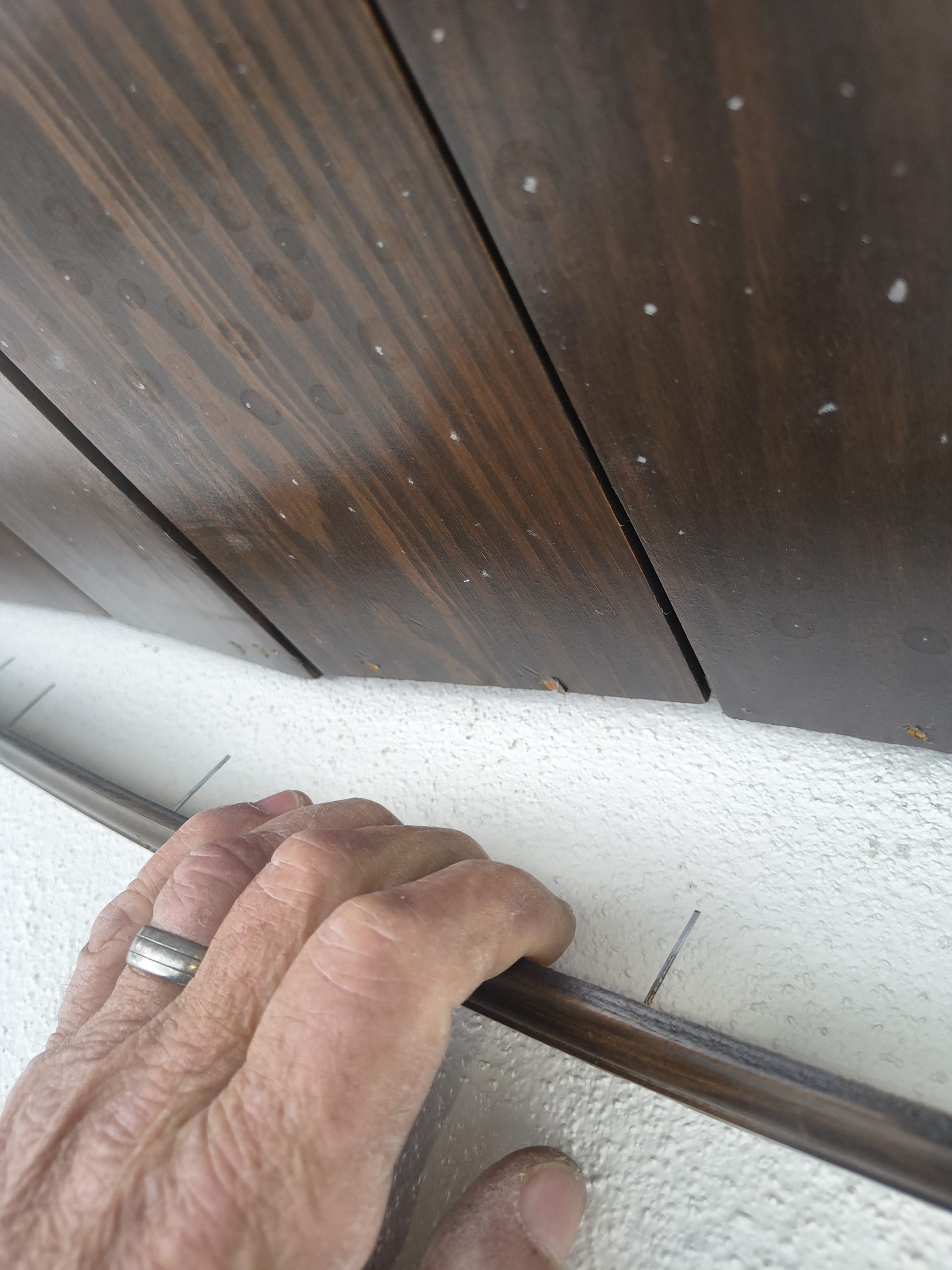 Tongue and groove boards buckling at a seam because of insufficient expansion clearance, with the carpenter's hand holding trim