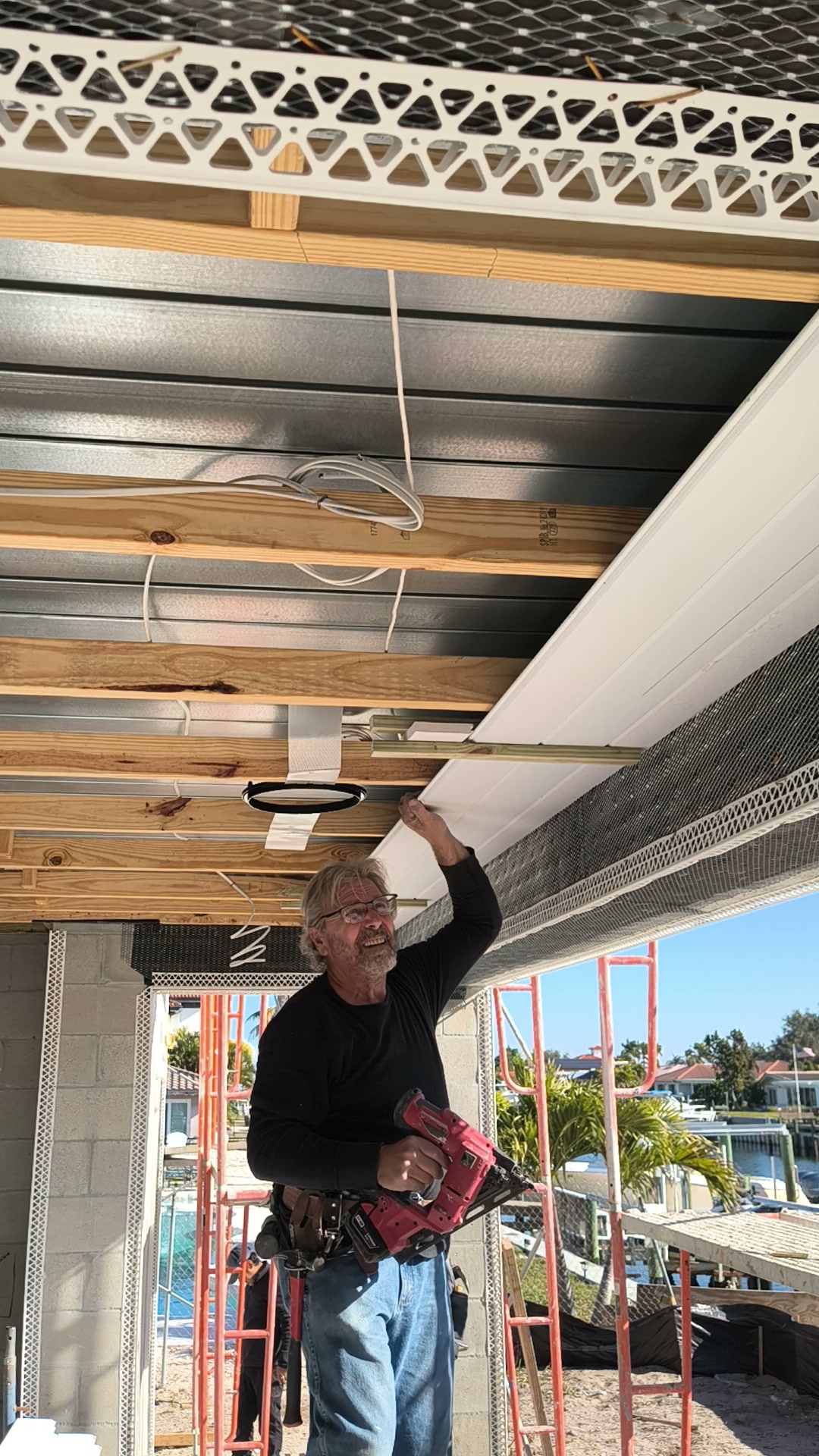 Herb checking white PVC tongue and groove ceiling boards with a finish nailer in his other hand